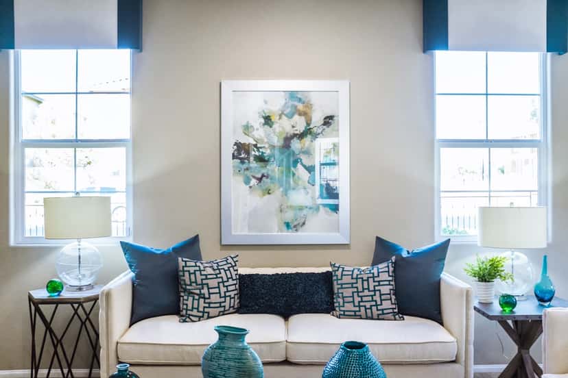 A large framed artwork centered above a white sofa between two bright windows